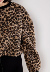 Pull en imprimé léopard marron et beige, fabriqué en tissu texturé. Présente des épaules déchues et un col noir côtelé.