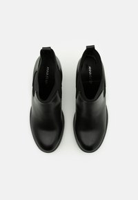 Botas de cuero negras hasta el tobillo con paneles laterales elásticos y una superficie lisa. Diseño de punta redondeada, estilo minimalista y suelas de goma planas.