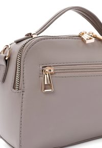 Grijze faux-lederen tas met gouden hardware, een ronde vorm, handvat boven, en een ritsvak aan de voorkant, met gestikte textuurdetails.