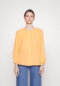 Blusa laranja de botão com decote redondo, mangas longas com punhos elásticos e corte descontraído. Feita de um tecido leve e texturizado.