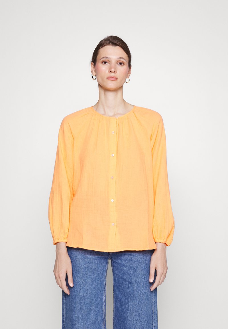 Blusa laranja de botão com decote redondo, mangas longas com punhos elásticos e corte descontraído. Feita de um tecido leve e texturizado.