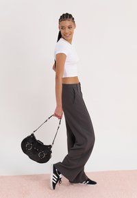 White cropped t-shirt, gray wide-leg pants, black handbag with metal accents, and black sneakers with white stripes. Soft pink background.