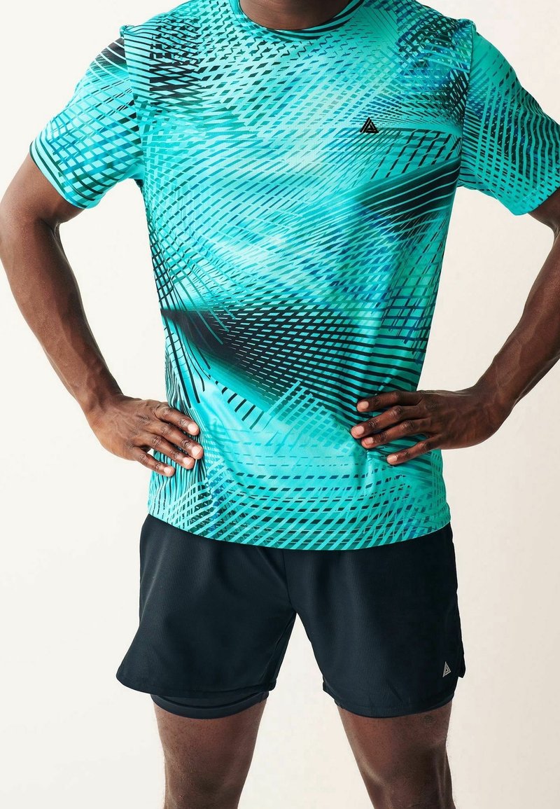 Camiseta deportiva de manga corta en un vibrante turquesa con patrones geométricos dinámicos en negro y verde azulado. Combinada con pantalones cortos deportivos negros.