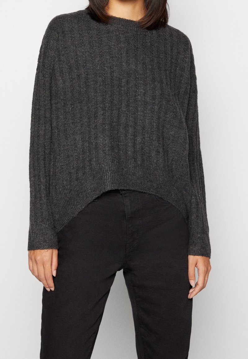 Pull en maille côtelée gris foncé avec une coupe ample, un col rond et un ourlet asymétrique. Tissu texturé, manches longues et aspect doux.