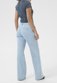 Jins flared denim berwarna biru muda dengan pinggang tinggi. Dilengkapi dengan dua saku belakang, tekstur halus, dan ujung yang dijahit. Dipadukan dengan atasan gelap yang pas.