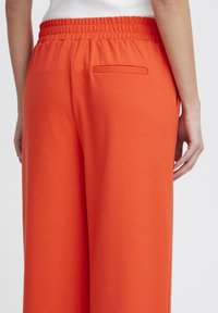 Oranje wijde broek met een gestructureerde stof. Beschikt over een elastische tailleband en een klein achterzakje. Glad ontwerp, casual stijl.