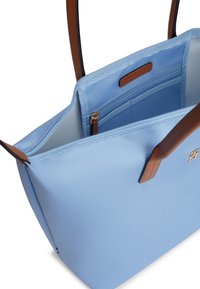 Τσάντα tote ανοιχτού γαλάζιου χρώματος με καφέ χειρολαβές, φερμουάρ στο πάνω μέρος, εσωτερική τσέπη με φερμουάρ και μικρό μεταλλικό λογότυπο στην μπροστινή πλευρά.