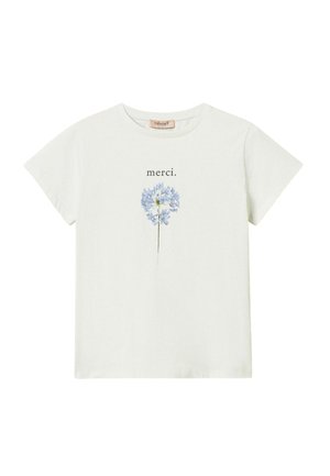 Giovane donna che indossa una t-shirt bianca con grafica, pantaloncini blu navy testurizzati, scarpe bianche slingback, tiene in mano una borsa blu navy con frange e catena dorata.