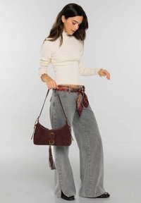 Suéter beige acanalado con puños con volantes, vaqueros grises de pierna ancha y un bolso de ante marrón con herrajes dorados y detalles de borlas.