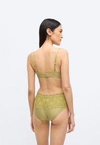 Oliivirohelisest pesukomplekt, millel on pitsiline ääris kõrge vöökohaga alusel ja sile siidriie rinnahoidjal reguleeritavate rihmadega.