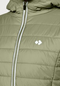 Veste matelassée vert clair avec fermeture éclair à l'avant et petit logo blanc sur la poitrine, présentant des coutures horizontales et un col rembourré.