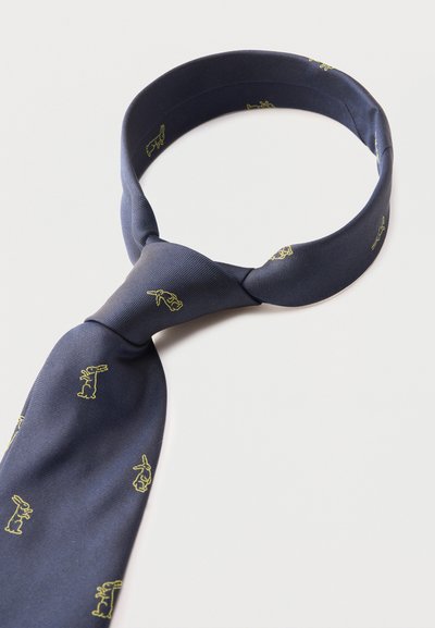 Corbata de seda azul marino con pequeños patrones de conejos amarillos, anudada de forma suelta y dispuesta en forma circular sobre un fondo blanco.
