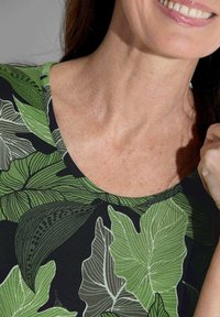 Zwarte top met een groen bladerenprint in verschillende tinten groen. De ronde halslijn en zachte textuur versterken het natuurlijke ontwerp.