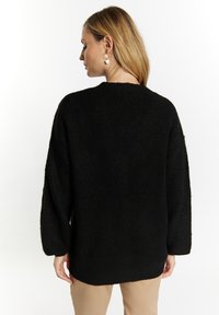 Zwart oversized trui met een zachte, gestructureerde afwerking, geribbelde zoom en brede mouwen. Kenmerkt zich door een achterkant die eenvoudig en naadloos is.