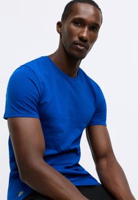 T-shirt in cotone blu con collo rotondo e maniche corte. Presenta una finitura leggermente testurizzata e un piccolo logo sull'orlo inferiore sinistro.