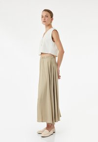 Vit kort ärmad linne topp med v-ringning och utan ärmar, kombinerad med en lång, flytande beige kjol och ljusa sk slip-on skor.