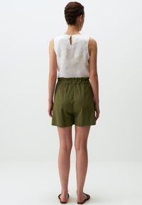Pantaloni corti in lino verde con vita elastica, abbinati a una maglietta bianca senza maniche con dettaglio a chiave sul retro.