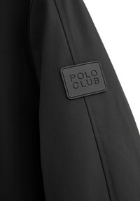 Giacca nera con tessuto testurizzato e cucitura visibile, evidenziata da un'etichetta in gomma quadrata con la scritta "POLO CLUB" sulla manica.