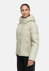 Giacca puffer beige chiaro con colletto alto e cappuccio regolabile. Presenta una chiusura con zip e tasche laterali con una texture liscia.