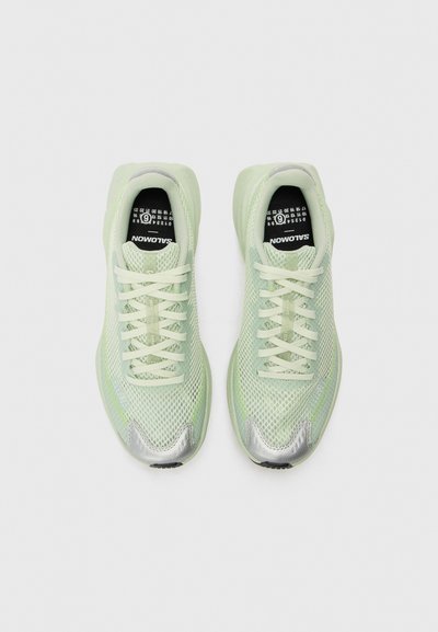 Hellgrüne Sportschuhe mit einem Obermaterial aus Mesh, reflektierenden silbernen Akzenten und flachen Schnürsenkeln. Text auf den Einlegesohlen liest "Salomon" und "NOWOTUS."