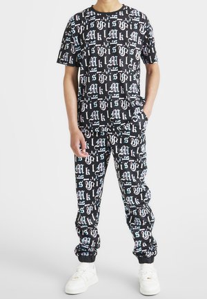Ensemble assorti noir comprenant un T-shirt et un pantalon, tous deux ornés d'imprimés typographiques colorés et variés. Le pantalon de survêtement possède des poignets élastiques et des poches.