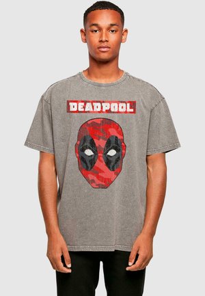 Grå oversized t-shirt med et rødt og sort camouflage Deadpool-grafik, der har hvide øjne og "DEADPOOL" tekst ovenfor.
