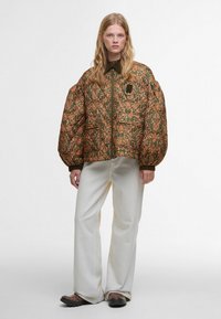 Casaco acolchoado com mangas oversized, apresentando um fundo verde e intrincados padrões florais laranja. Fecho éclair, complementado por um bolso.