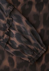 Leopardenmuster-Stoff in Brauntönen und Schwarz. Mit gekräuseltem Rand und elastischer Manschette, samt einer glatten, weichen Textur.