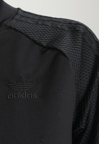 Svart träningslinne med en texturerad mesh-design på axlarna och en subtil broderad logotyp. Slät tygkvalitet med en åtsittande passform.