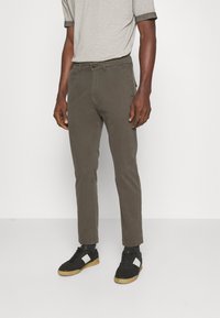 Olivgröna byxor med slim fit, tillverkade av ett mjukt material. Matchade med svarta sneakers med vita detaljer och gummisulor.