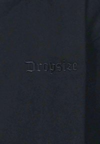 Schwarzer Stoff mit geprägtem Text "Dropsize" in einer stilisierten Schriftart, mit matter Oberfläche und subtiler Textur.