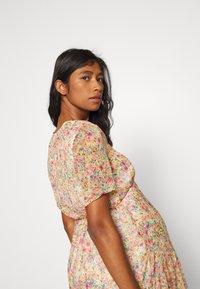 Vestido floral feito de tecido leve, com mangas curtas em formato de puff, em cores pastel, e um padrão espalhado de flores em rosa, amarelo e verde.