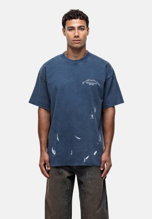 Blauwe oversized katoenen T-shirt met een ronde halslijn, verouderde details en een bedrukte logo op de borst. Gecombineerd met donkere denim broek.