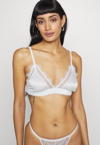 Bralette branco em satin com acabamento em renda, apresentando uma forma triangular, alças ajustáveis e uma faixa elástica franzida na base.