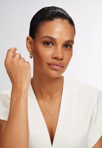Bijoux en or comprenant un collier délicat avec une petite médaille, un bracelet assorti et des boucles d'oreilles créoles, portés par une personne.