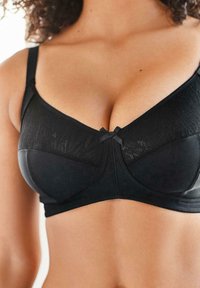 Reggiseno nero con tessuto strutturato e motivo floreale, spalline regolabili e un piccolo dettaglio a fiocco nero al centro.