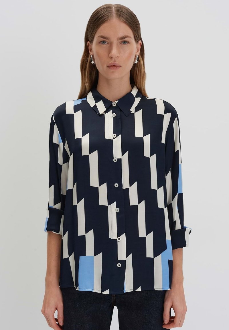 Camicia blu navy con motivi geometrici bianchi e azzurri, maniche lunghe, colletto classico e chiusura con bottoni. Tessuto morbido e leggero.