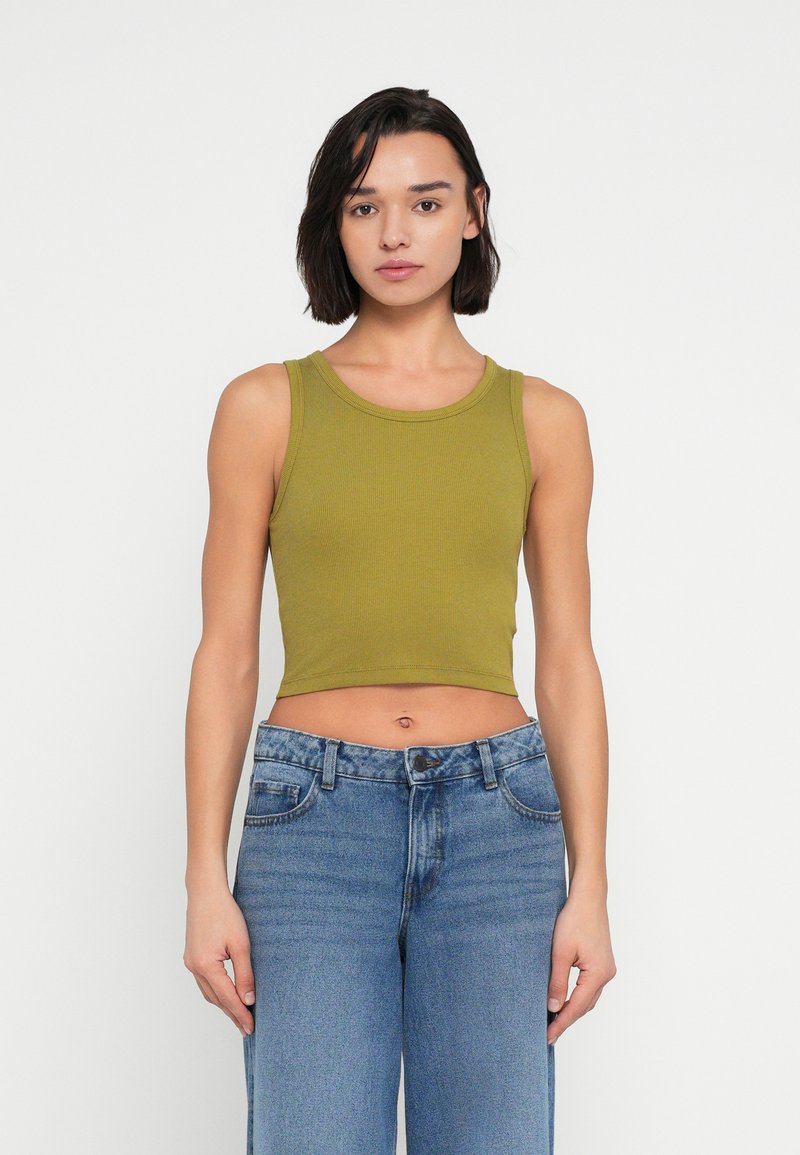 Ελιά πράσινο ριμπ crop top με στρογγυλή λαιμόκοψη, σε συνδυασμό με ανοιχτό μπλε τζιν παντελόνι με φαρδιά μπάρα, με κλασικό κούμπωμα με κουμπιά και φερμουάρ.