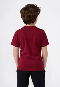 Burgundy bomulls t-shirt, korta ärmar, rund halsringning, slät textur, enfaldig bakvy, bärs med svarta byxor.