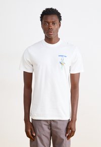 T-shirt bianca in cotone con colletto girocollo, caratterizzata da una grafica colorata di Bugs Bunny e il testo "Carhartt WIP" sul petto.