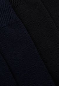 Zwei Paar Socken: eines in dunklem Marineblau und das andere in Schwarz. Strukturierter Strickstoff mit glatter Oberfläche und geripptem oberen Rand.