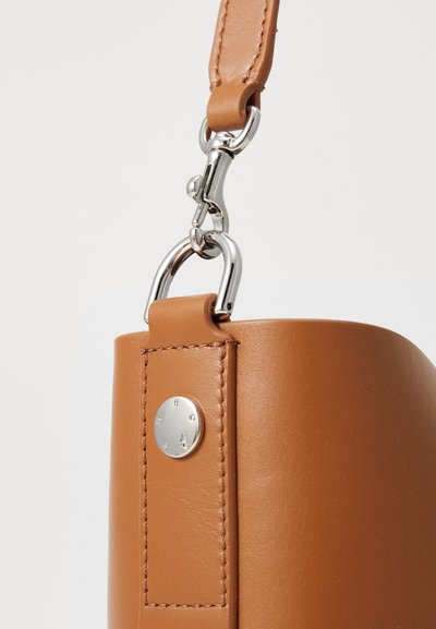 Brown leather handbag with a rounded shape, metal hardware accents, and a textured surface, featuring a silver attachment clip.