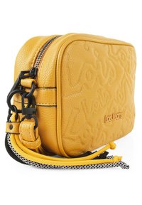 Bolso cruzado de cuero texturizado amarillo con logo embosado, doble cremallera y acentos de cordón coloridos. Forma rectangular compacta.
