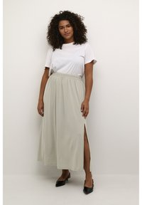 Light beige maxi skirt with an elastic waistband and side slits, made from a soft material. Paired with a white t-shirt and black flats.