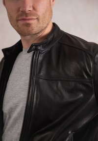 Black leather jacket with a stand-up collar, showcasing a smooth texture, zip closure, and stitch detailing, layered over a gray shirt.