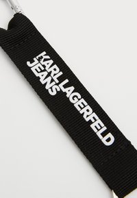 Black fabric strap with "KARL LAGERFELD JEANS" printed in white. Features a metallic clasp and a textured weaving pattern.