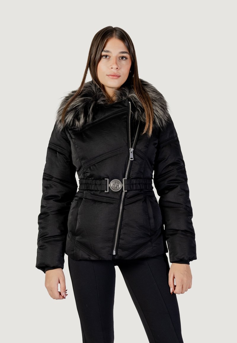 Giacca a vento nera con colletto in pelliccia sintetica, chiusura con zip, cintura con fibbia decorativa e texture trapuntata. Il modello indossa pantaloni neri.