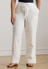 Fehér, széles szárú lenv ászon nadrág húzózsinóros derékrésszel és két oldalzsebbel, könnyű, texturált anyagból. Barna szandálokkal viselve.