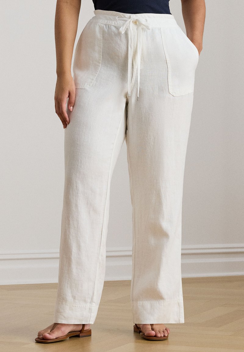 Fehér, széles szárú lenvászon nadrág húzózsinóros derékrésszel és két oldalzsebbel, könnyű, texturált anyagból. Barna szandálokkal viselve.