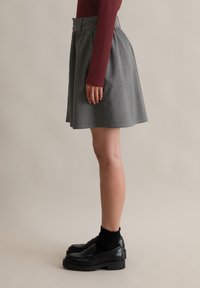 Szürke csíkozott szoknya magas derékkal és ráncolt részletekkel, fekete mokaszinokkal és bordó, bordázott, hosszú ujjú felsővel párosítva.